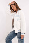 White Women's Bomber Jacket with light blue embroidery, casual sweatshirt style with striped ribbed trim, paired with denim cargo pants.